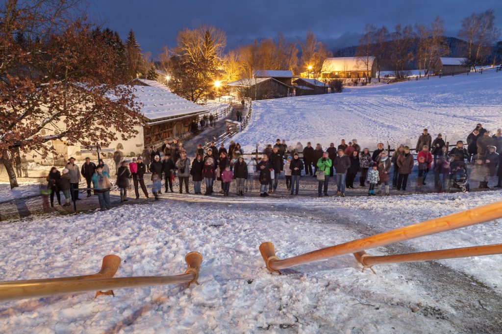 Eine Menschenmenge steht auf einem Weg und lauscht Alphornbläsern.