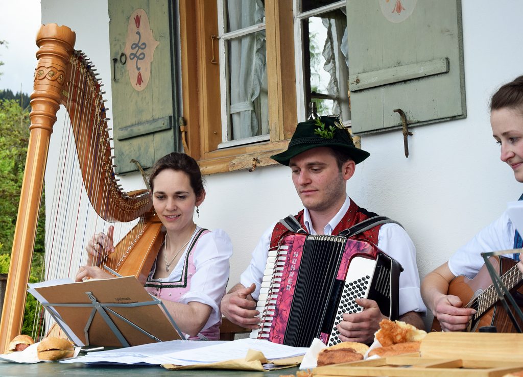Es musizieren eine Frau mit Harfe, ein Mann mit Akkordeon und eine weitere Frau mit Gitarre.